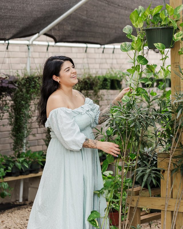 Gabriela, owner of Sweetie Loaves, smiling among hanging plants